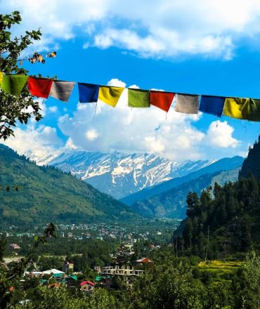 Charming view of Manali village with Himalayan mountains and colorful prayer flags in summer.